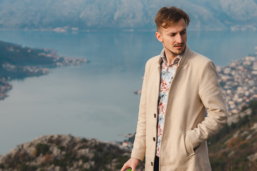 Waist-up portrait of a handsome young man looking over the sea from high above. He is a tourist on vacation.