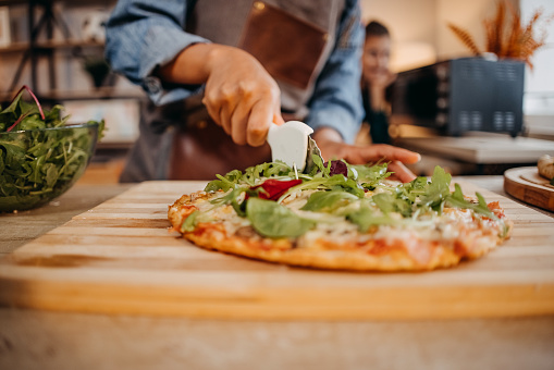 Closeup of a hand cutting delicious freshly baked pizza with a roller