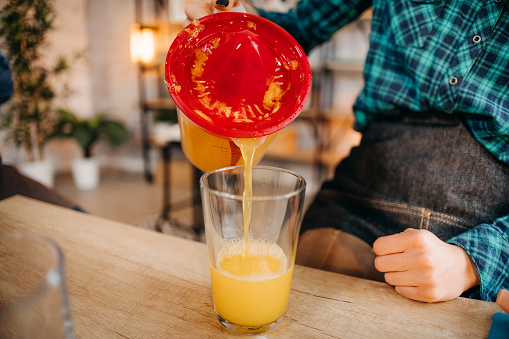 Close-up of a woman's hand pouring orange juice into a glass.