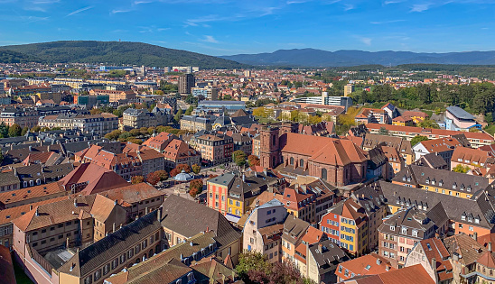 View of the historical part of the city of Belfort with a fortress, tiled roofs of houses, a cathedral and mountains in the background. Belfort, France - September 2022