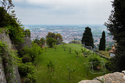 Bergamo, Italy - May 4, 2022: Aerial view over the city of Bergamo from San Vigilio mountain. Small football court on edge of the hill.