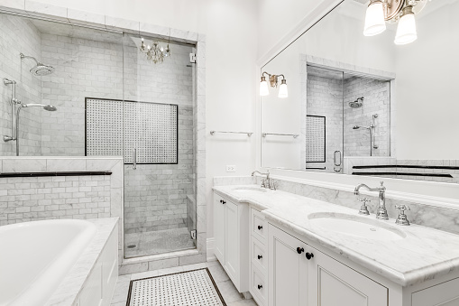 A luxurious white bathroom with a marble counter top, hot tub tub, and a stand up shower with custom tiles.