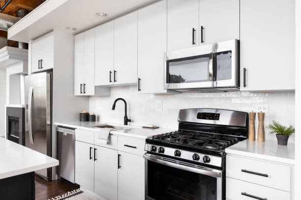 A white kitchen with stainless steel appliances. A loft kitchen with white cabinets, exposed wood ceiling, and stainless steel appliances. stove stock pictures, royalty-free photos & images