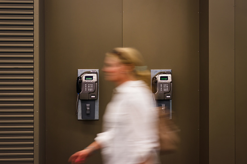 Woman in motion blur passing at public coin operated pay phone. Old telephone on the wall