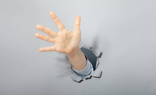 istock The woman's hand shows with a gesture that everything call for help. Torn hole in gray paper. 1454680041