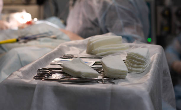 手術用滅菌器具は、外科医と助手が患者の手術を行う手術台の前のトレイにあります。手術器具のセットがテーブルの上にあります。 - 縫合糸 ストックフォトと画像