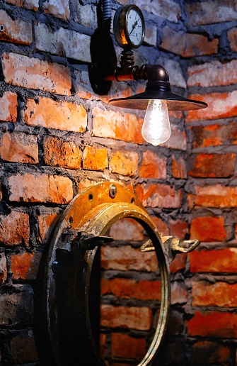 A vertical shot of steampunk style interior design lamp and mirror over red brick wall background