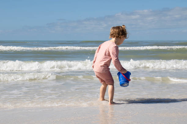 Little girl walking on a beach through the water.