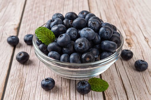 Ripe blueberry in a glass bowl over wooden background. Fresh blueberries for vegetarian dessert. Wild berry for natural antioxidant and healthy eating concept. Vitamin vegan snack. Front view.