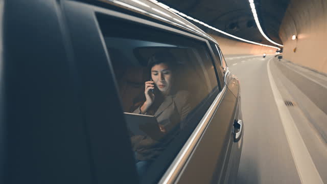 Asian Chinese businesswoman talking over phone at back passenger seat on the move at night in city