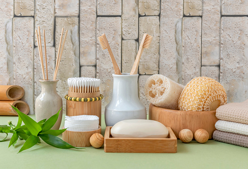 Bamboo bathroom accessories. Toothbrush, cotton swabs, cotton pads, soap dish, soap, towel, loofah and sisal washcloth. Body care. Green bamboo background. Stop plastic.