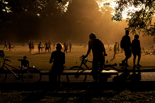 Silhouette of bike riders resting, and of a group of teenager having playing soccer on the background under the twilight sunset sky in a public park.
