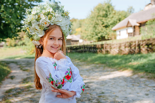 Little girl wearing Ukrainian national dress and wreath of flowers outdoor. Portrait of teenager in folk authentic dress with embroidery against rural view. A symbol of faith in peace for all Ukrainian people.
