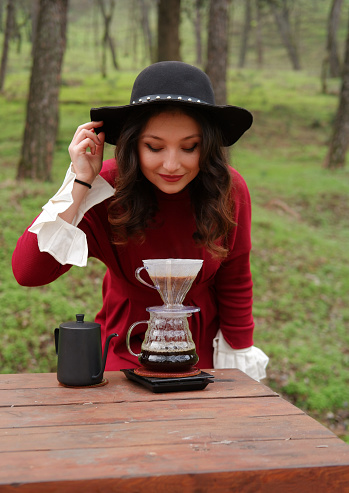 Young Asian woman preparing and drinking hot coffee in the forest.