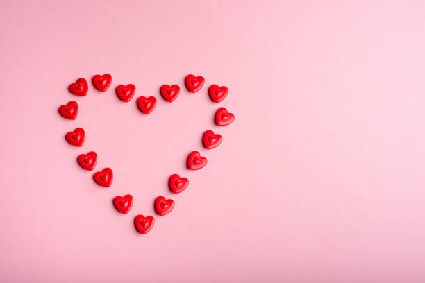 istock Heart-shaped frame made with small hearts on a pink background. 1454705506