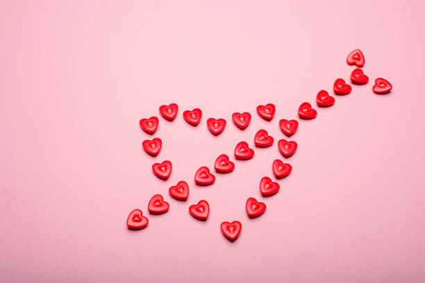 istock Heart-shaped frame made with small hearts crossed with an arrow on a pink background. 1454705512