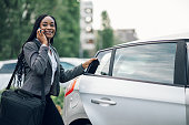 African american business woman getting into the car and using smartphone