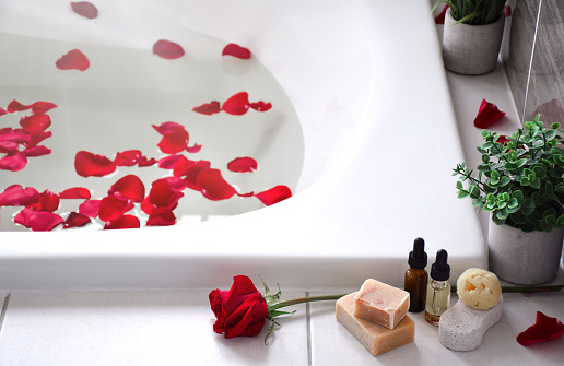 Red rose with personal toiletries on the edge of bathtub filled with red rose petals