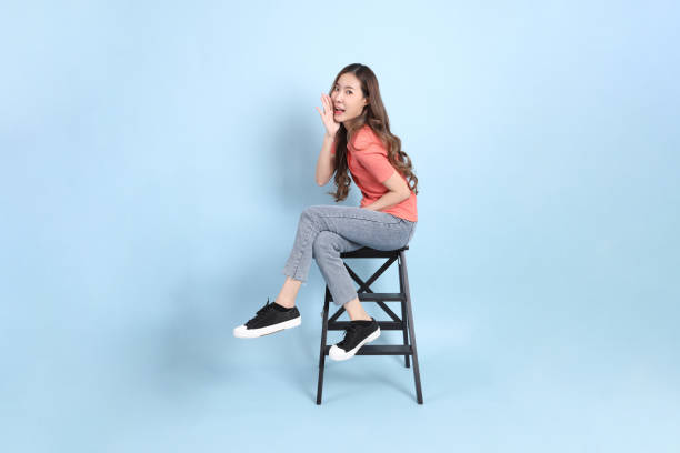 The young adult Asian woman with casual clothes with jeans sitting on the blue background.
