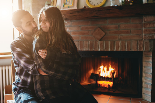 A young couple in love is resting near a fireplace at home. They are spending quality time together for Saint Valentine Day.