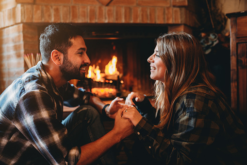 A young couple in love is resting near a fireplace at home. They are spending quality time together for Saint Valentine Day.