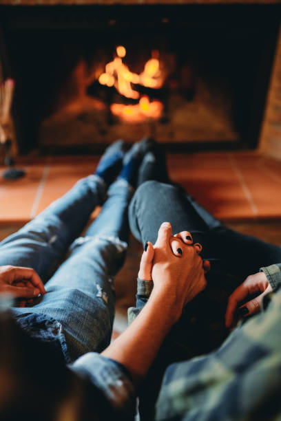 A romantic couple is holding hands in front of the fireplace at home stock photo