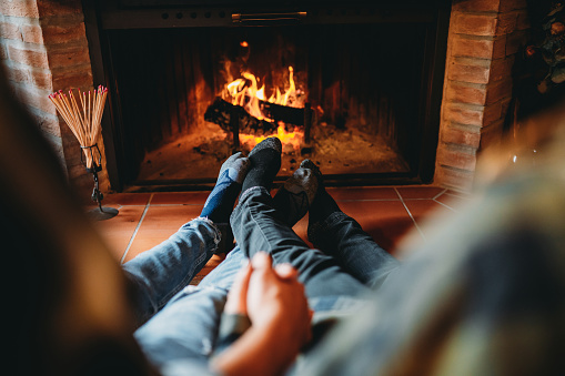 A romantic couple is holding hands in front of the fireplace at home. Resting cozy day at home during Saint Valentine Day.