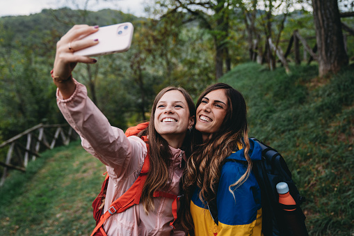 A young adult couple is taking a selfie during a mountain vacation. They are hiking together.