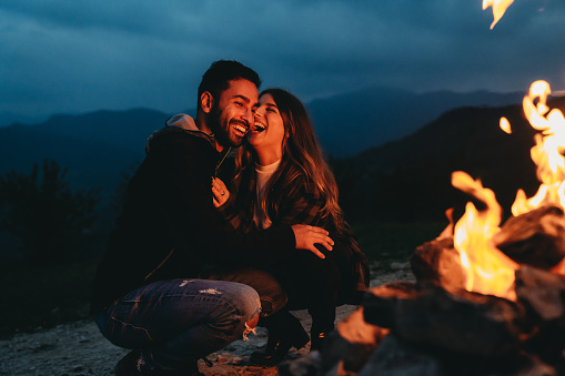 A romantic couple is spending time together near a fireplace outdoor. Fireside outdoor in the mountain.