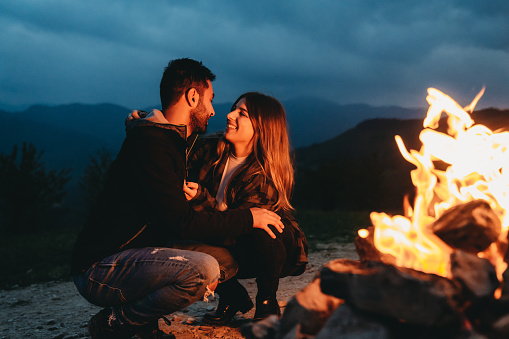 A romantic couple is spending time together near a fireplace outdoor. Fireside outdoor in the mountain.