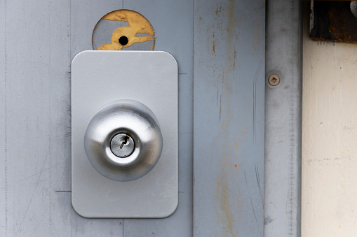 A front view image of a newer metal doorknob on an old wooden grey door.