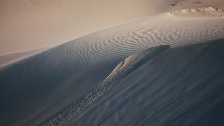 Wide shot of sand blowing across desert dunes during wind storm with warm afternoon light