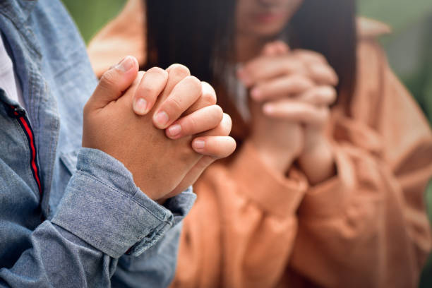 istock Hands folded praying over a Bible. Casual man praying with his hands together over a closed Bible, 1454732039