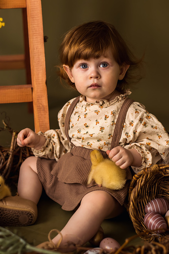 Cute red-haired little girl in vintage dress playing with duckling in Easter decorations.Spring and Easter concept.