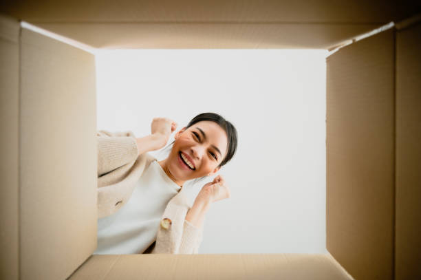 istock Surprised young asian woman unpacking. Opening carton box and looking inside. Packaging box, delivery service. Human emotions and facial expression 1454749671