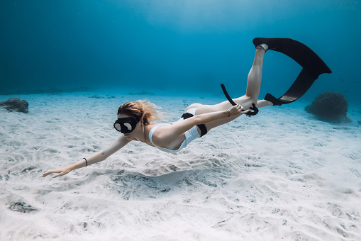 Woman freediver in white swimwear dive and exploring sea life. Freediving in tropical blue ocean