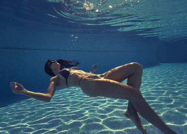 istock Young slim brunette woman wearing bikini posing motionless inside the pool on the depth, underwater 1454766103