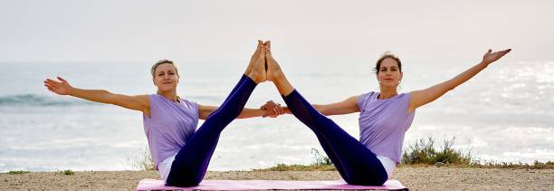 istock Two women doing acro yoga  twisted boat pose exercise at the beach 1454766636