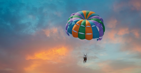 Two people enjoy parasailing flight during sunset bright colorful sky background