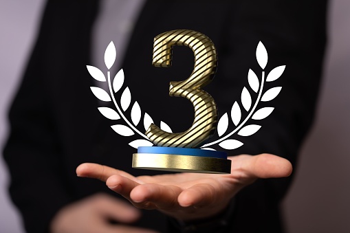 A 3D rendering of a third place golden award a male hand holding on a blurry background