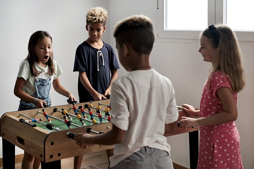 A Group of multi-cultural cute children spending playtime with friends playing foosball together.