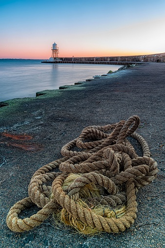 A vertical shot of a rope at the coast on the background of a lighthouse near Helsingborg, Sweden