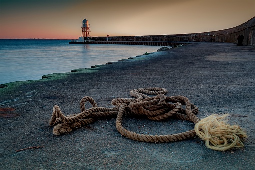 A rope at the coast on the background of a lighthouse during sunset near Helsingborg, Sweden