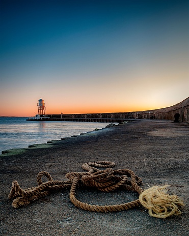 A rope at the coast on the background of a lighthouse during sunset near Helsingborg, Sweden