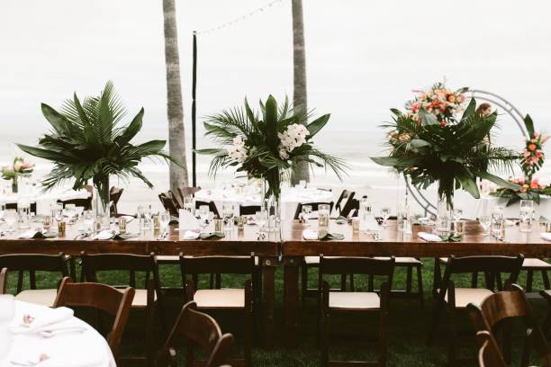 istock Table with green tropical floral arrangements at a beach wedding 1454770203