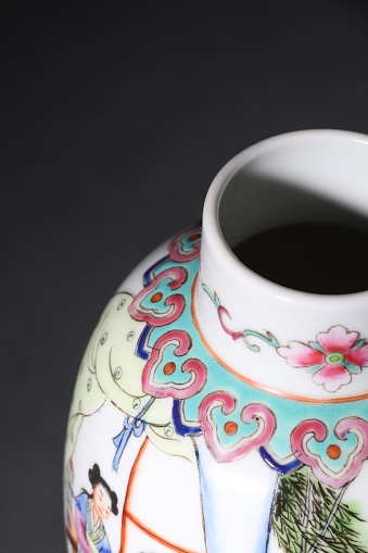 A vertical shot of a traditional painted Chinese vase with a dark background