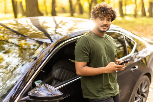 istock Successful indian man standing by his car texting on mobile phone 1454776164