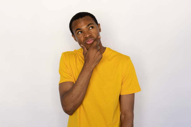 istock Thoughtful young man  holding fingers on his chin looking away 1454777540