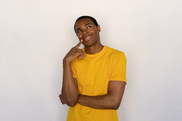 istock Dreamy young man holding finger on his chin looking away 1454777545