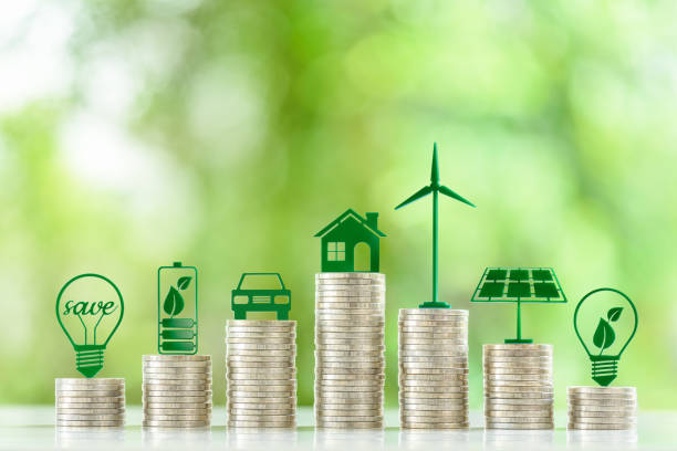 precios y costos de generación de energía renovable o limpia, concepto financiero: símbolos ecológicos verdes sobre pilas de monedas, por ejemplo, bombilla de bajo consumo, una batería, un panel de células solares, una turbina eólica. - alternative energy data fuel and power generation light bulb fotografías e imágenes de stock